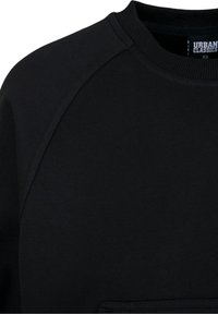 Gros plan d'un sweat-shirt noir à col rond montrant la couture de l'épaule et le col côtelé avec une étiquette de la marque Urban Classics à l'intérieur.