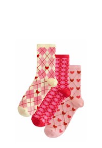 Drei Paar gestrickte Socken: Eine mit einem cremefarbenen und rosafarbenen Argyle-Muster, eine einfarbig in Pink und eine mit roten Herzen auf einem hellrosa Hintergrund.