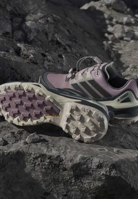 Двойка лилави и черни туристически обувки Adidas Terrex с издръжливи гумени подметки Continental, поставени на скалист терен.