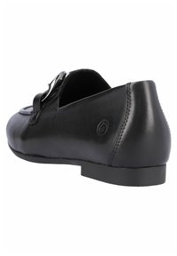 Zapato plano de cuero negro con punta redondeada, detalle de correa decorativa y hebilla, y suela de goma baja y plana. Textura suave con acentos de costura.