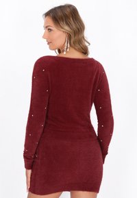 Burgunderfarbene Strickkleid mit langen Ärmeln, das eine weiche Textur aufweist und mit kleinen Strasssteinen entlang der Ärmel verziert ist.