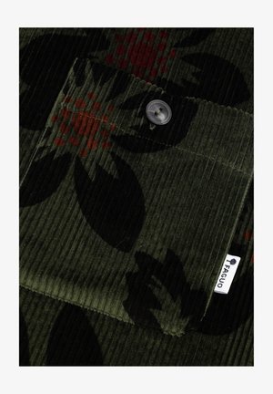 Tessuto di corduroy verde con un motivo floreale arricchito da dettagli in rosso e arancio. Include un dettaglio con bottone e una piccola etichetta del marchio.