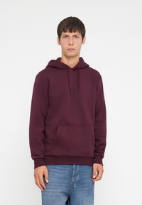 Bordeauxkleurige pullover hoodie met een verstelbare capuchon, een voorzak en geribbelde manchetten. Gekoeld met lichtblauwe spijkerbroek.