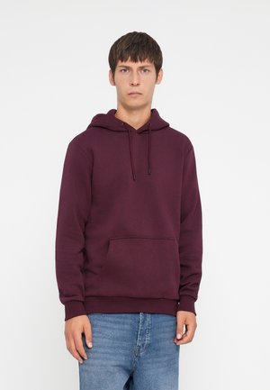 Sweatshirt à capuche maroon avec cordon de serrage ajustable, poche avant et poignets côtelés. Associé à un jean en denim bleu clair.