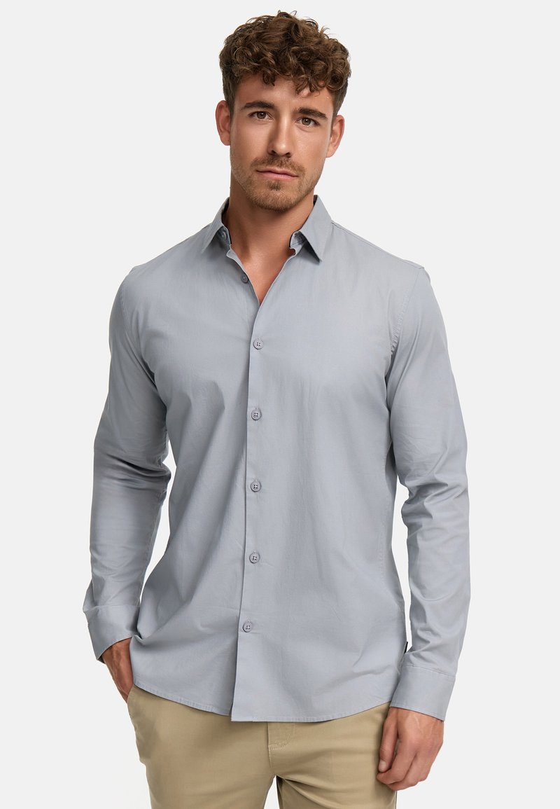 Camisa de botones de manga larga en gris claro, con ajuste slim, que presenta un cuello clásico y cinco botones en la parte delantera. Tejido de algodón suave.