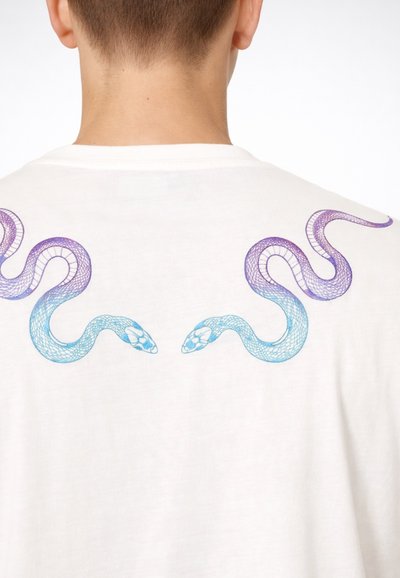 Vista posteriore di una persona che indossa una maglietta bianca con due serpenti viola e blu rivolti l'uno verso l'altro stampati vicino alle spalle.