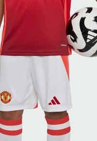 Röd träningströja med orangea detaljer, vita shorts med Manchester United-logotyp, Adidas-logotyp och rödrandiga strumpor.
