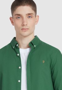 Groene overhemd gemaakt van katoen. Heeft een klassieke kraag, witte knopen en een klein gouden logo op de linkerkant van de borst. Draag het over een wit T-shirt.