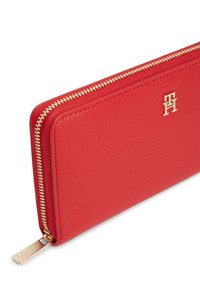 Κόκκινο δερμάτινο πορτοφόλι με υφή, με χρυστό φερμουάρ και μικρό χρυσό λογότυπο στη μία πλευρά. Ορθογώνιο σχήμα.