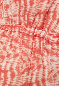 Röd- och vitmönstrat tyg med skrynklig textur. Har rynkad sömnad längs midjan, vilket skapar en avslappnad passform.
