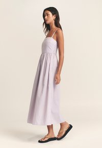 Šviesiai violetinė dryžuota maxi suknelė su aptemptu liemeniu ir surinkta juosmeniu. Taip pat plonos petnešėlės ir laisvai krentanti sijono dalis, dėvima su lygiais sandalais.