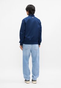 Ναυτικό μπλε μπουφάν με ψηλό γιακά, ελαστικούς καρπούς και τελείωμα. Φορεμένο πάνω από ανοιχτού μπλεφάρσες, με κίτρινες και σκούρες αθλητικές μπότες.