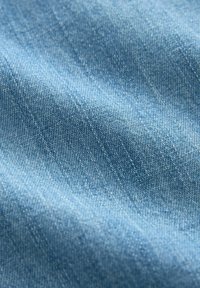 Tissu en denim bleu clair présentant une texture lisse avec de subtils motifs de tissage diagonal et de légères variations de couleur sur l'ensemble.