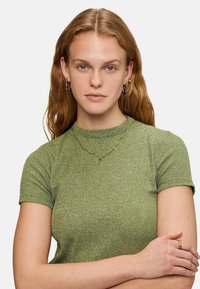 Grön randig kortärmad topp i ett texturerat material, matchat med ett halsband med vågmönster i guld och hoopsörhängen.