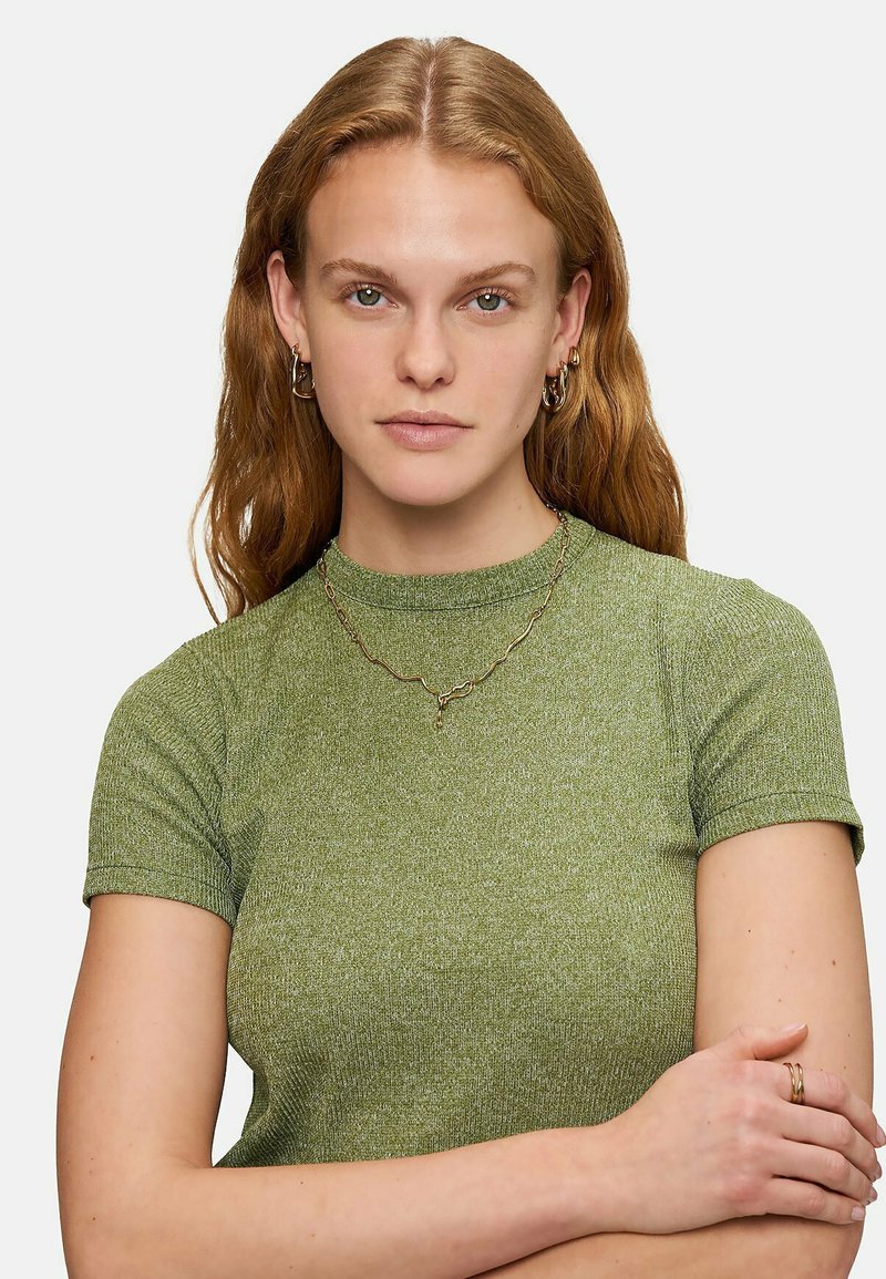Grön randig kortärmad topp i ett texturerat material, matchat med ett halsband med vågmönster i guld och hoopsörhängen.