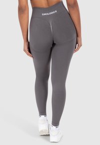 Graue, hochtaillierte Leggings mit strukturierten Akzenten, die ein Logo am Bund haben. Der Stoff sieht glatt und figurbetonend aus.