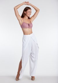 Rood en wit gestreepte strapless crop top, gecombineerd met vloeiende witte broek met zijscheuren, geaccentueerd met open-teende schoenen.
