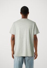 Šedé bavlněné tričko s krátkým rukávem, rovný střih a kulatým výstřihem. Má hladkou texturu a minimalistický design.