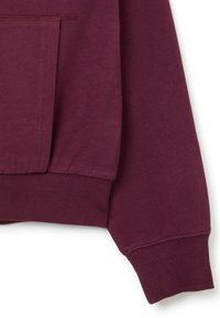Felpa color bordeaux con polsini e orlo a costine. Presenta una tasca a marsupio e una texture liscia. Focalizzarsi sui dettagli di cucitura di alta qualità.