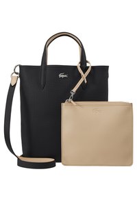 Sac fourre-tout noir en synthétique avec des accents crème, deux poignées, une sangle détachable, et une pochette beige zippée avec une surface texturée. Logo Lacoste présenté.