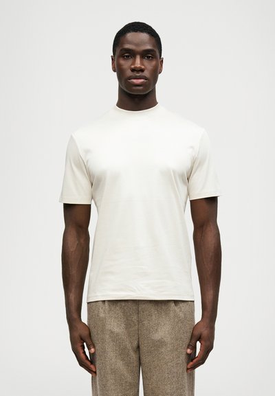 Short-sleeve, crew-neck t-shirt in light beige cotton. Features a smooth texture and a relaxed fit, paired with patterned trousers.