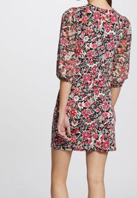 Mini-robe fleurie avec une superposition noire transparente ornée de fleurs rouges et roses, des manches bouffantes et un corsage ajusté.