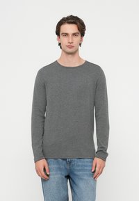 Siva majica z dolgimi rokavi, zaobljenim izrezom in mehko teksturo, kombinirana s svetlo modrimi jeans hlačami. Udoben in sproščen kroj.