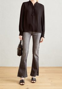 Blusa nera a maniche lunghe con scollatura a volant, abbinata a jeans grigi a zampa d'elefante con orli sfilacciati e sandali neri con zeppa.