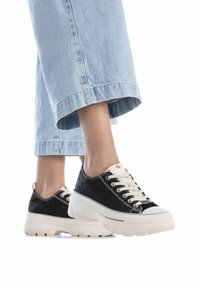 Zapatillas de mezclilla oscura con suelas de goma blanca, parte superior texturizada, puntera redonda y cordones en contraste. Combinándolas con unos vaqueros de pierna ancha en azul claro.