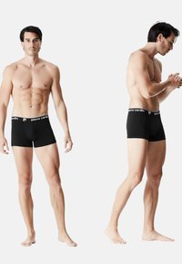 Boxers en coton noir pour hommes avec une ceinture à logo blanche, dotés d'un design ajusté et d'une texture lisse. Présentés de face et de côté.