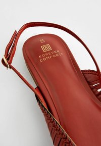 Sandale en cuir rouge avec un design de bride tissée, semelle plate et marquage doré. La sangle cheville ajustable ajoute du détail. Taille 40 indiquée à l'intérieur.