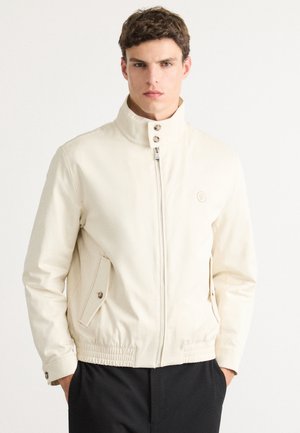 Ljusbeige jacka med hög krage, framdragkedja och sidofickor. Har elastiska manschetter och ett figursytt midjeband för en skräddarsydd look.