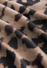 Tissu doux avec des taches noires irrégulières sur un fond brun clair, ressemblant à un motif léopard.