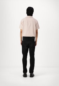 Camisa de manga corta a rayas en rosa claro y blanco, combinada con jeans negros. Zapatos negros completan el atuendo. Detalles de costura visibles.