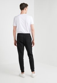 Svarta joggerbyxor med en bakficka, rundade muddar och elastisk midja, kombinerat med en enkel vit T-shirt och vita sneakers.