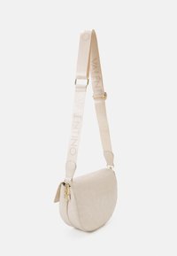 Béžová kožená kabelka ve tvaru půlměsíce přes rameno s širokým nastavitelným popruhem, na kterém je embosovaný nápis "VALENTINO", a detaily ve zlatém tónu.