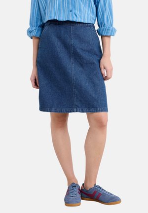 Vrouw die een blauwe denimrok draagt, een blauw gestreept overhemd met knopen en opgerolde mouwen, en blauwe sneakers met rode strepen.