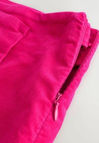 Fuchsia corduroy fabric with a visible zipper and pocket. The texture is ribbed, enhancing its softness and tactile quality.