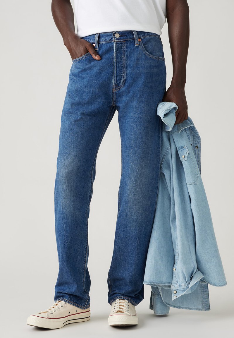 Light blue denim jeans with a straight leg design, medium wash, five pockets, contrasting stitching, worn with a light blue shirt.