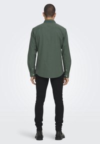 Groene knoopshirt met een gebogen zoom, gemaakt van stof, met lange mouwen en een kraag, gecombineerd met zwarte slim-fit broek en laarzen.