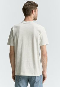 Tricou din bumbac gri deschis, cu o suprafață texturată, mâneci scurte și un guler clasic rotund. Croială casual, fără grafică sau modele vizibile.