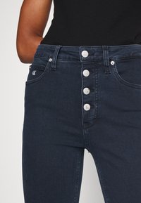 Mörka denim jeans med hög midja som har femknapps gylf, subtil logodetalj och klassiska fickor med en smidig textur.