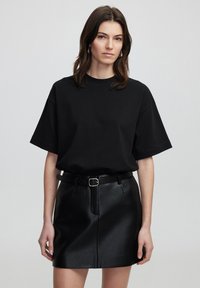Zwart katoenen oversized t-shirt met korte mouwen, gecombineerd met een zwarte nep leren minirok met een voornaad en riem.