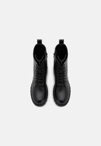 Bottines en cuir noir avec une finition lisse, présentant un cordon frontal, une fermeture éclair sur le côté et des semelles en caoutchouc robustes pour plus de durabilité.