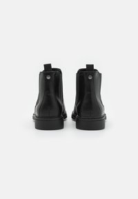 Bottes basses en cuir noir avec une finition lisse, des coutures minimales, et des languettes à l'arrière pour un enfilage facile. Semelles en caoutchouc plates.