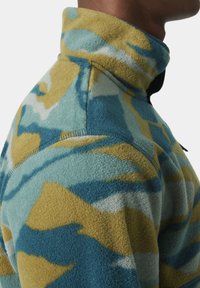 Sudadera de forro polar con un cuello alto que presenta un patrón abstracto en azul, verde y amarillo. Textura suave con costuras visibles y detalles de diseño.