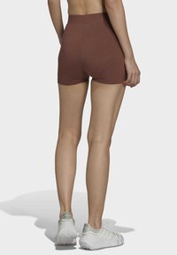 Hnedé šortky s vysokým pásom vyrobené z elastického materiálu, majúce hladkú textúru a priliehavý strih, skombinované s svetlými športovými topánkami.