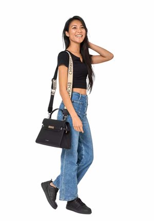 Jeune femme portant un crop top noir et un jean, marchant en souriant, avec un sac à main noir à bandoulière beige brandée sur l'épaule.
