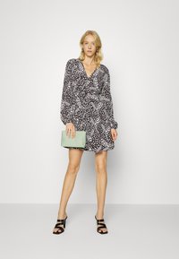 Vestido preto e branco com padrão, decote em V e mangas longas e bufantes. Combinado com uma bolsa de mão verde menta e sandálias pretas de salto.