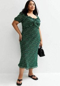 Groene bloemen midi-jurk met balonmouwen, geraffineerde halslijn, aansluitende silhouet en een zoom die onder de knie valt; gedragen met zwarte platte sandalen en tas.